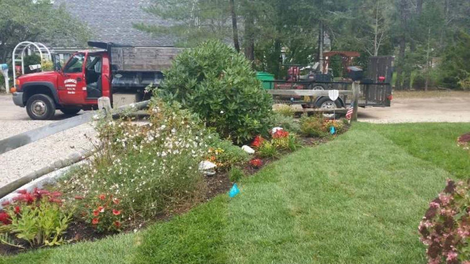 Landscaping truck and trailer parked behind a planted flower bed and fresh sod