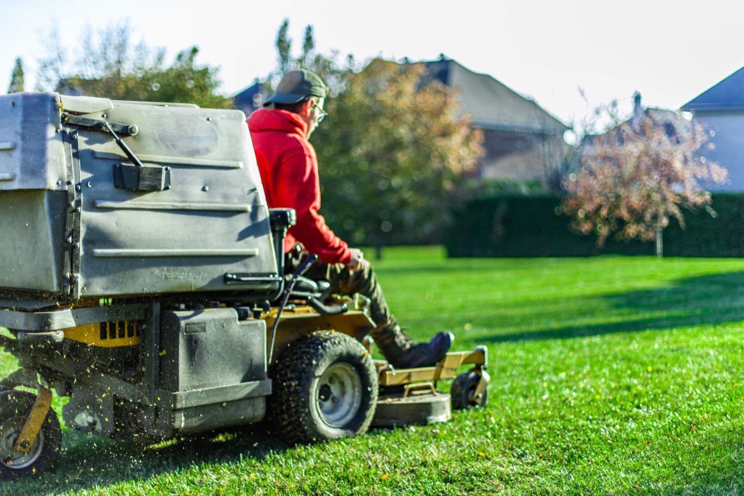 Landscaper mowing a lawn on a riding mower with a grass collector